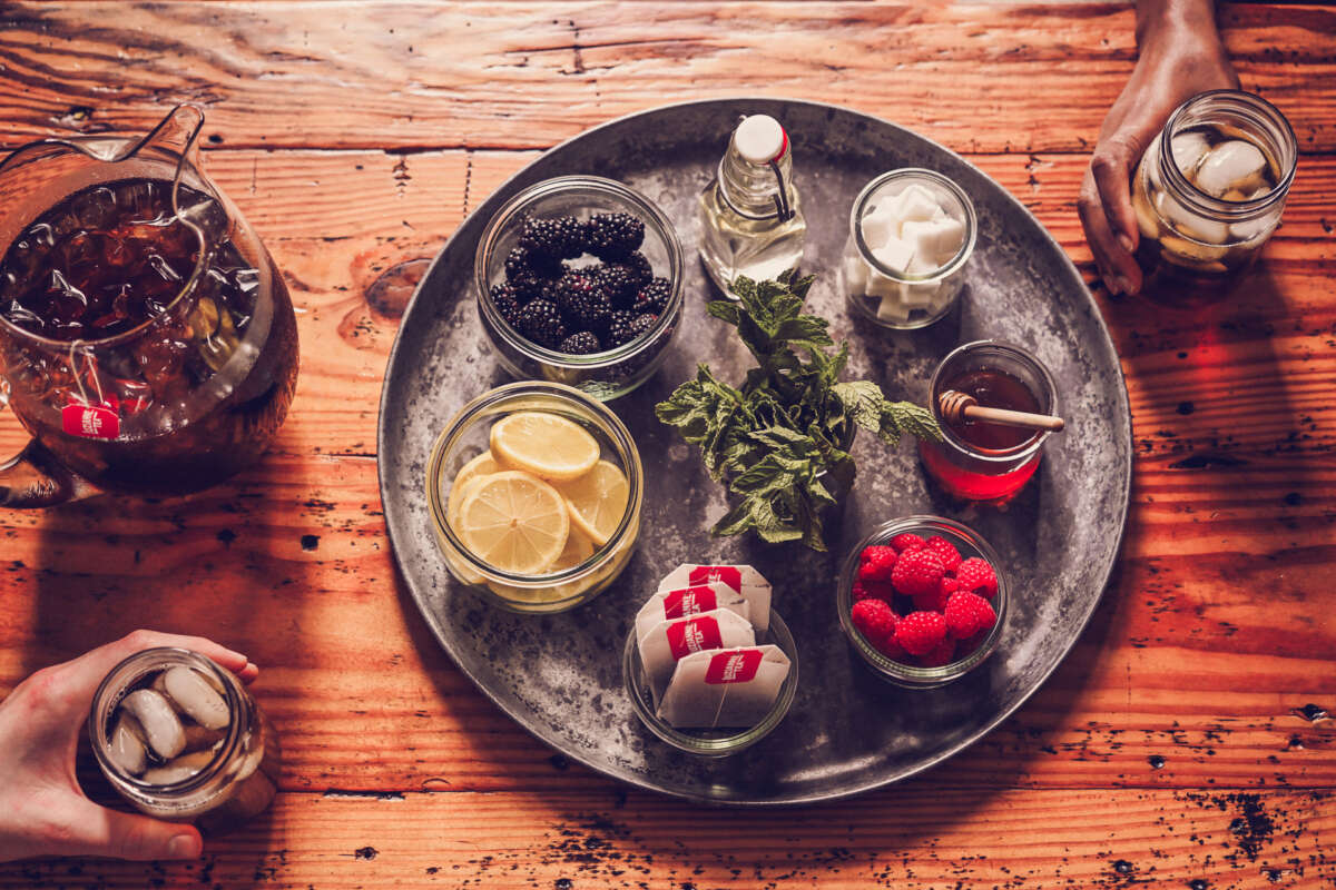 Flavorings for Luzianne Iced tea on a metal tray that include mint, simple syrup, raspberries, sugar cubes, blackberries, honey and lemon slices