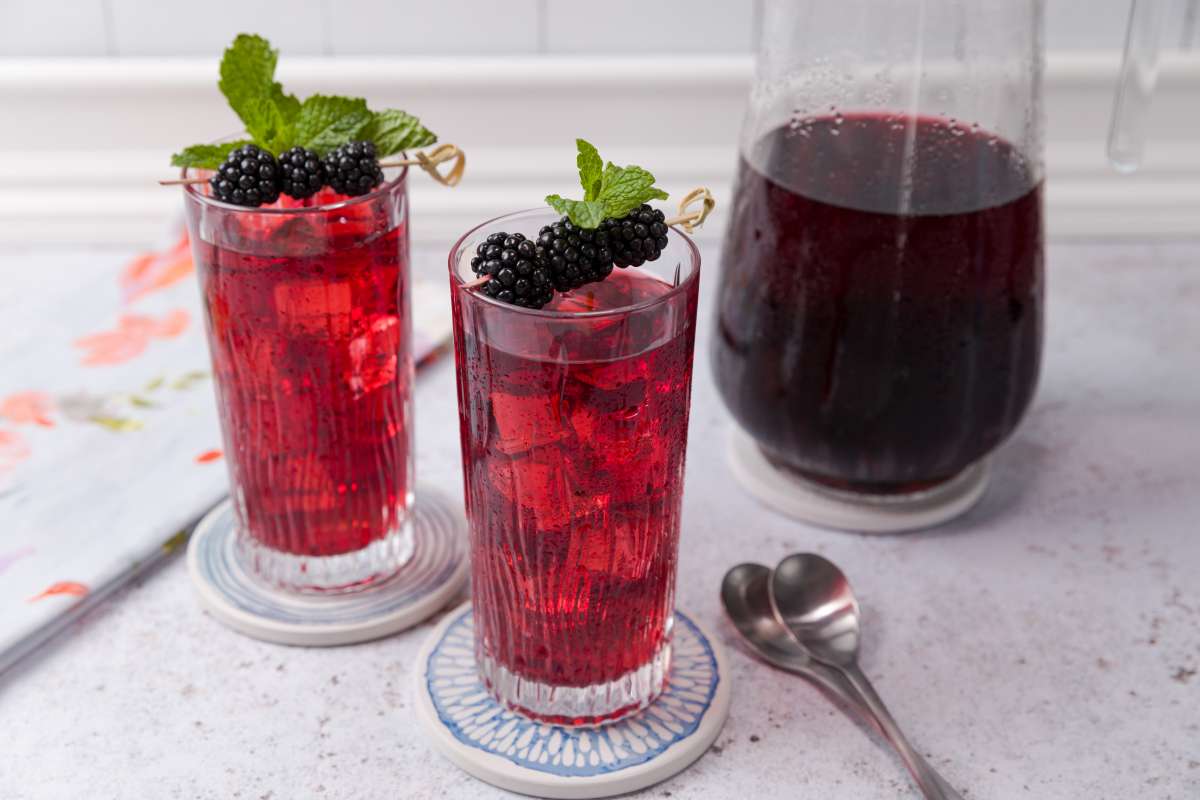 Tall glasses of Luzianne Hibiscus Iced Tea infused with blackberry and garnished with fresh mint leaves