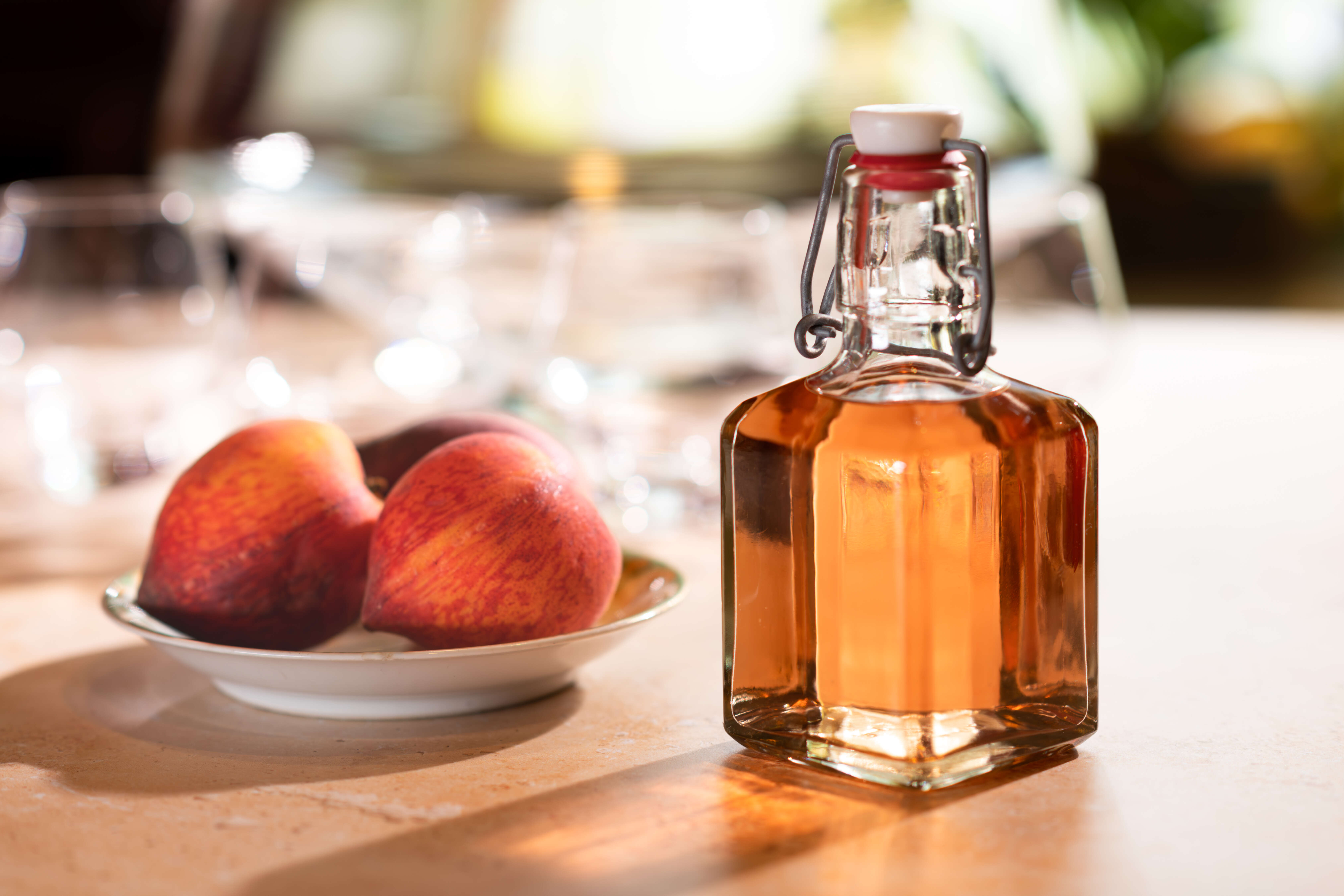 Bottle of homemade Spiced Peach Syrup next to a dish of fresh peaches