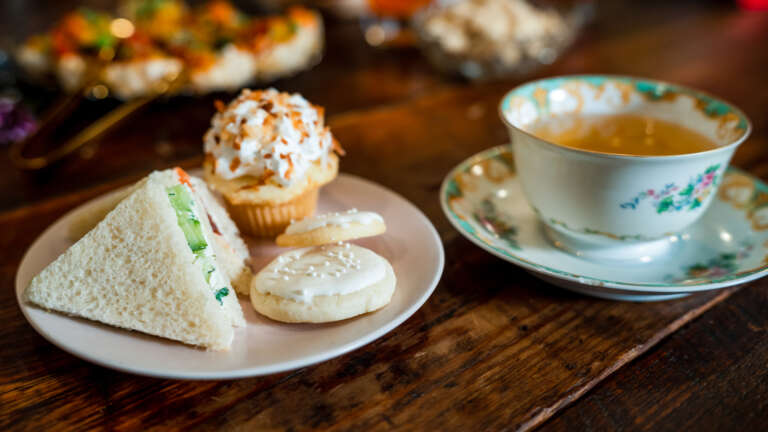 A tea party plate laden with cucumber and watercress triangle sandwich, mini coconut cupcake and homebaked tea cookies. 