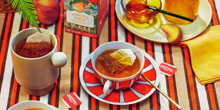 Brightly colored tea cup of Southern Blends Honeyed Peach Tea with box of tea in background